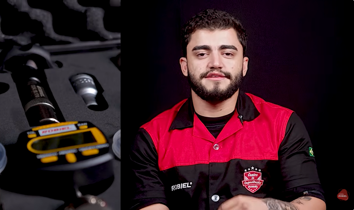 Instrutor da ROBIEL de uniforme preto e vermelho com logotipo Centro de Capacitação, olhando para a câmera durante depoimento em vídeo, fundo escuro de estúdio, ao lado peças e ferramentas de injeção diesel desfocadas, iluminação suave, fotografia realista