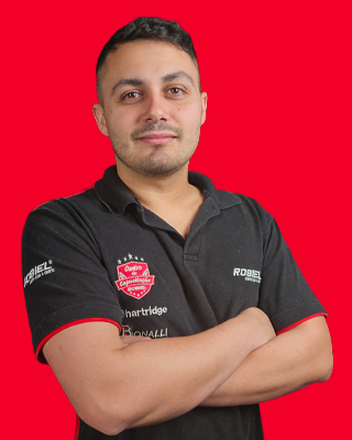Foto profissional de instrutor especialista em Common Rail da ROBIEL, homem com braços cruzados, uniforme polo preto com logotipos ROBIEL e Chartridge, fundo vermelho vibrante, retrato em estúdio, expressão confiante